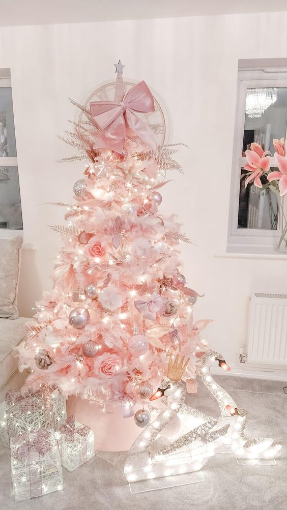 a blush Christmas tree with blush and metallic ornaments, pink leaves, crowns and a pink bow on top is amazing