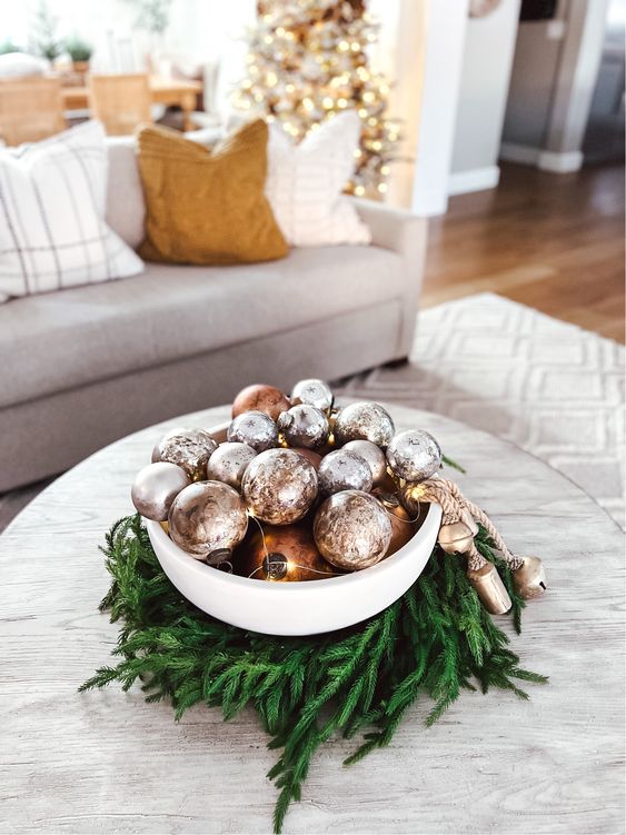 a bowl surrounded with evergreens, with copper and silver ornaments and lights plus bells is a catchy and cool idea
