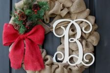 a burlap wreath with a monogram, a red bow and evergreens and pinecones for a chic look