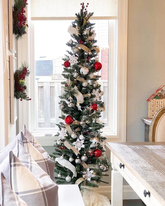 a classic slim Christmas tree styled with ribbons, silver and red ornaments, snowflakes and bells is lovely
