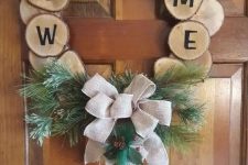 a cool rustic Christmas wreath of tree slices with letters, evergreens, bells and a large burlap bow is an awesome decor idea