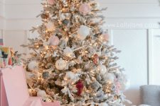 a flocked Christmas tree decorated with blush and white ornaments, grey pompoms and lights is amazing