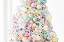 a flocked Christmas tree decorated with candy-colored ornaments that cover the whole tree