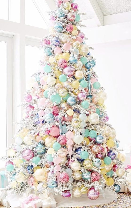 A flocked Christmas tree decorated with candy colored ornaments that cover the whole tree
