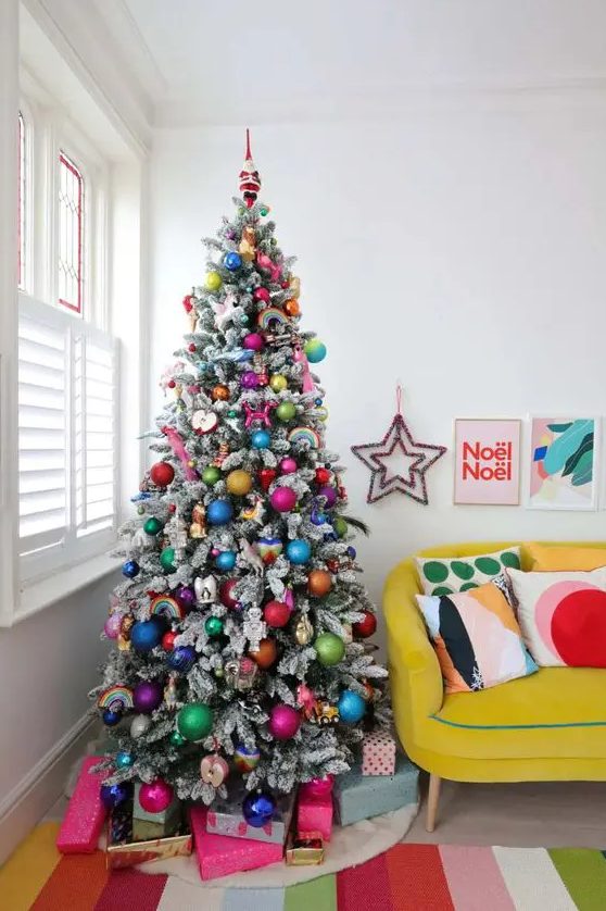a flocked Christmas tree decorated with super colorful ornaments and rainbows is a gorgeous idea for a bold space