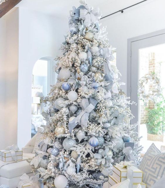 a flocked Christmas tree fully covered with pastel blue ornaments, ribbons, branches and bows is a chic idea for the holidays