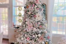 a flocked Christmas tree styled with pink, blusha nd pearly ornaments, oversized faux flowers and ribbons