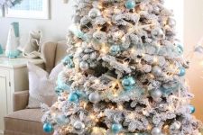 a flocked Christmas tree with lights, silver and tiffany blue ornaments, snowy pinecones and starfish is a fresh idea for a beach Christmas space