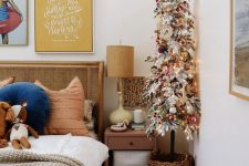 a flocked pencil Christmas tree with lights, colorful pompoms and ornaments placed in a basket
