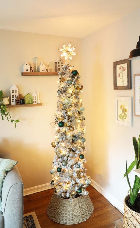 a flocked pencil Christmas tree with silver, gold and dark green ornaments, lights and plaid ribbons