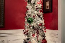 a flocked pencil Christmas tree with white, red and green ornaments, lights, ribbons and snowflakes