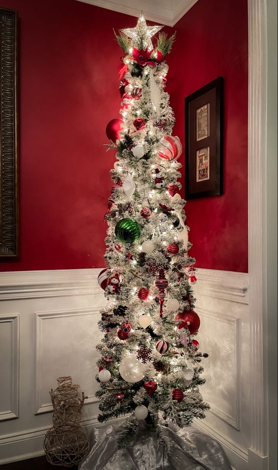 a flocked pencil Christmas tree with white, red and green ornaments, lights, ribbons and snowflakes