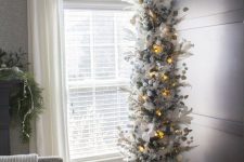 a flocked skinny Christmas tree with lights, snowballs, branches, faux blooms and leaves looks unusual