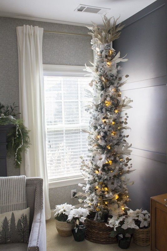 a flocked skinny Christmas tree with lights, snowballs, branches, faux blooms and leaves looks unusual
