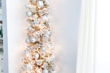 a flocked slim Christmas tree with white tinsel and silver ornaments plus lights is a delicate and catchy idea