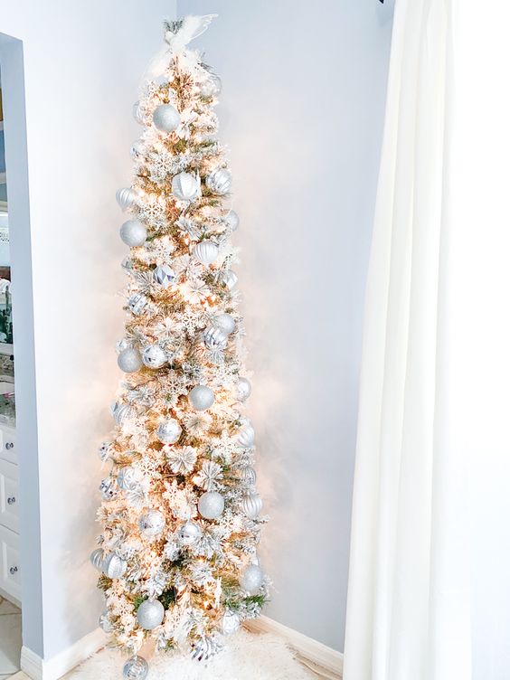 a flocked slim Christmas tree with white tinsel and silver ornaments plus lights is a delicate and catchy idea