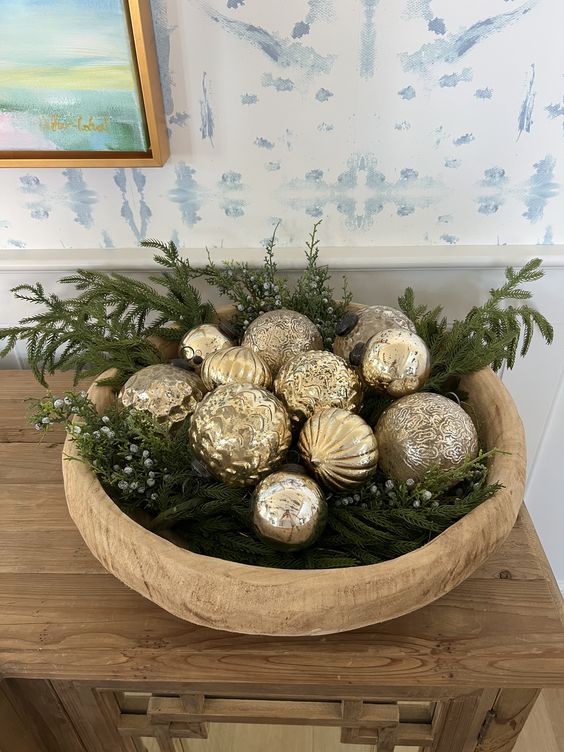 a glam Christmas arrangement of a wooden bowl with evergreens and gold ornaments is a lovely idea