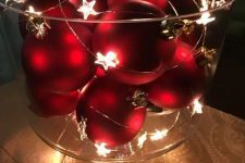 a glass bowl with red Christmas ornaments and a star light garland is a cool winter decoration