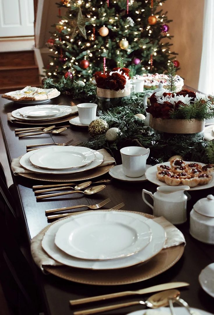 a gorgeous christmas tea party table with evergreens and red and white blooms, elegant white porcelain and delicious sweets