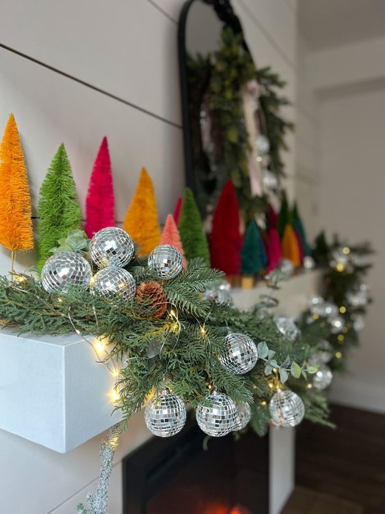 a holiday mantel with evergreens, lights, silver disco balls, colorful bottlebrush Christmas trees is awesome