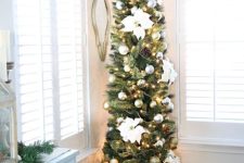 a lovely and subtle pencil Christmas tree with lights, silver ornaments, faux blooms and pinecones plus a star topper