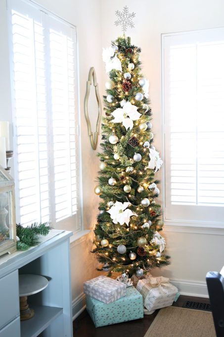 a lovely and subtle pencil Christmas tree with lights, silver ornaments, faux blooms and pinecones plus a star topper