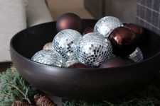 a modern Christmas arrangement in a black bowl, with disco balls and burgundy ornaments, with evergreens and pinecones