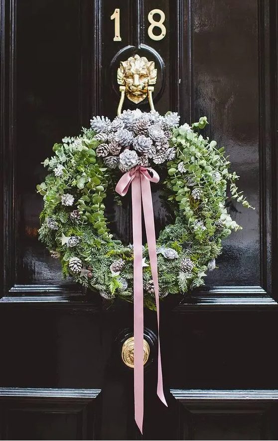 a modern Christmas wreath of greenery, evergreens, snowy pinecones and a pink ribbon bow is a cool idea