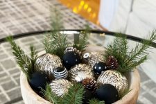 a modern glam Christmas centerpiece of a wooden bowl with black and gold ornaments, evergreens is a lovely idea