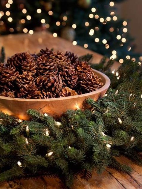 a pinecone Christmas centerpiece of a wooden bowl, pinecones, an evergreen wreath with lights is cozy and natural