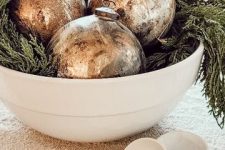 a pretty Christmas centerpiece of a bowl with evergreens and vintage Christmas ornaments is a beautiful idea