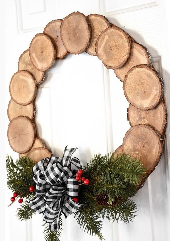 a pretty and cozy rustic Christmas wreath of tree slices, evergreens, berries, a buffalo check bow is a cool decoration