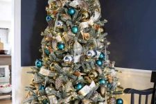 a pretty woodland glam Christmas tree with green, teal, gold ornaments, shiny metallic pinecones, a white printed ribbon and some deer ornaments