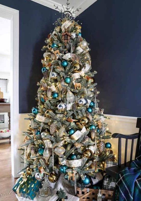 a pretty woodland glam Christmas tree with green, teal, gold ornaments, shiny metallic pinecones, a white printed ribbon and some deer ornaments