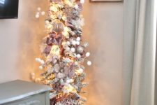 a refined pencil Christmas tree of silver tinsel, with pink and silver ornaments, faux blooms, snowballs and lights