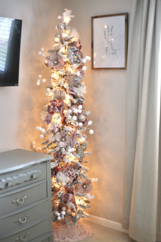 a refined pencil Christmas tree of silver tinsel, with pink and silver ornaments, faux blooms, snowballs and lights