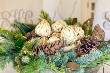 a rustic Christmas centerpiece of a wooden bowl, evergreens, pinecones and artichokes is a cozy rustic decor idea