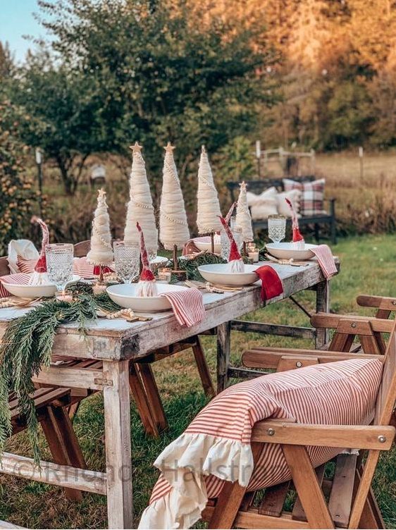 a rustic Christmas tablescape with evergreens, faux Christmas trees, red and striped napkins and mini gnomes in each place setting