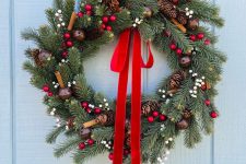 a rustic Christmas wreath of evergreens, cinnamon, bells, berries and a large ribbon bow
