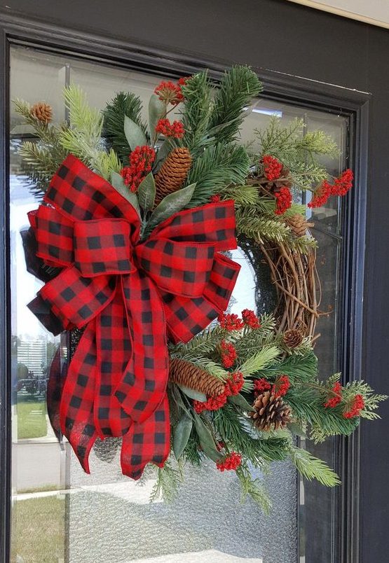 a rustic Christmas wreath with evergreens, red berries, pinecones and a red plaid bow is a lovely decoration to rock
