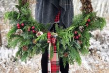a rustic Christmas wreath with evergreens, snowy pinecones, red berries and a red plaid bow is a lovely decoration to make