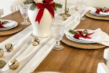 a simple and elegant Christmas table setting with white textiles, red and white roses, bells, woven placemats