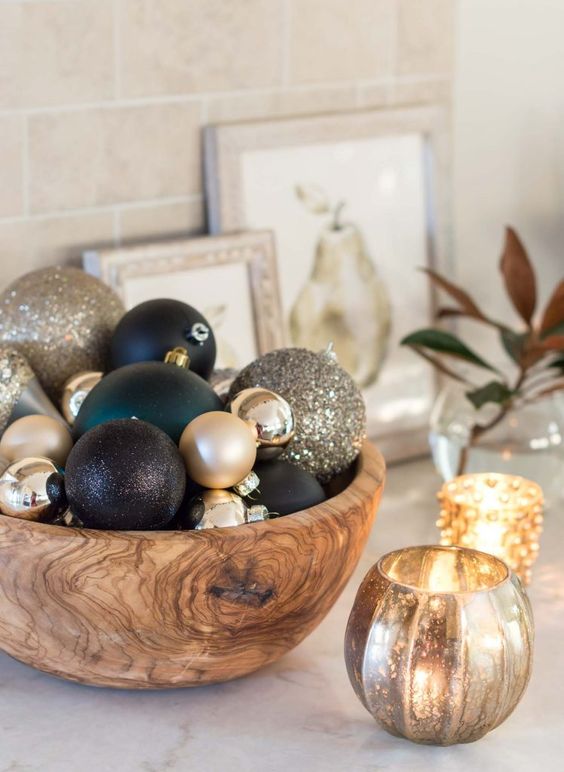 a simple glam Christmas centerpiece of a wooden bowl with gold, black and dark green ornaments of various sizes