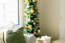 a skinny Christmas tree decorated with silver and orange ornaments is a catchy idea for a cozy modern space