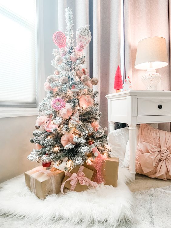 a small and pretty flocked Christmas tree with pink and blush ornaments shaped as sweets, lights and candy tree topper