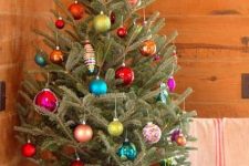 a small natural tree in a bucket decorated with colorful ornaments looks bold and eye-catching
