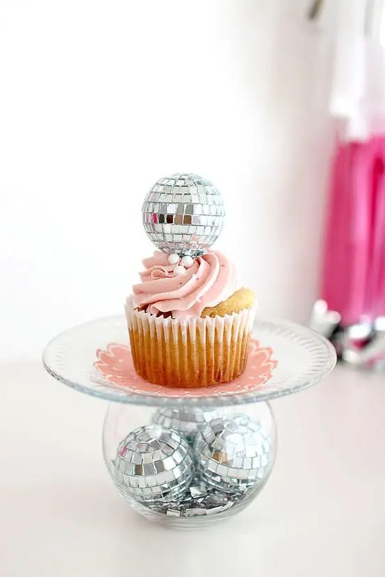a stand of a bowl with disco balls, a sheer plate and a cupcake topped with a disco ball for a party feel