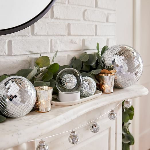 a stylihs NYE mantel with greenery, disco balls, candleholders and a disco ball garland hanging