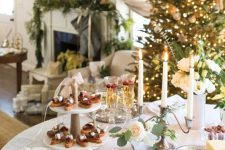 a stylish Christmas tea party table with all kinds of sweets and cookies served here, candles and blooms and greenery in a vase