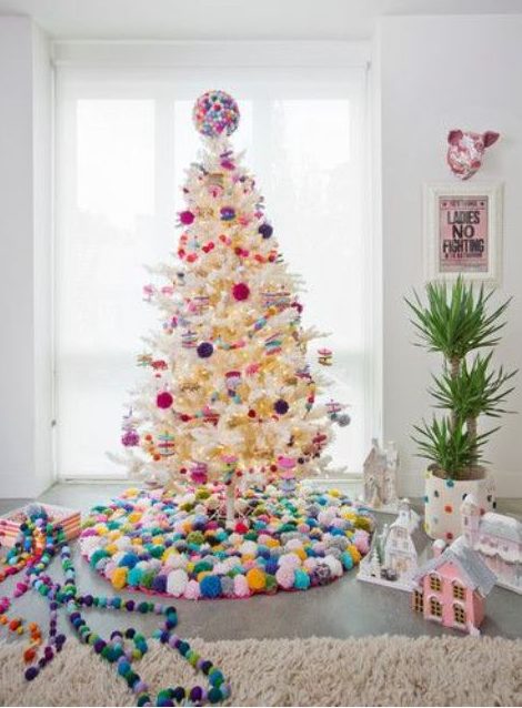 a white Christmas tree decorated with bold pompom ornaments and with a colorful pompom tree skirt and a ball on top